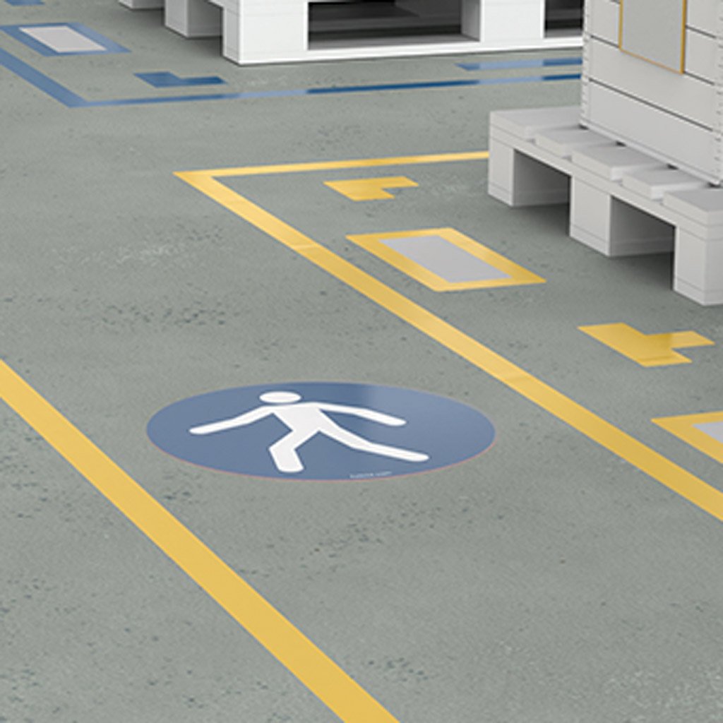 Custom directional floor graphics and signs in an industrial setting, featuring directional arrows and a safety symbol on a grey floor.