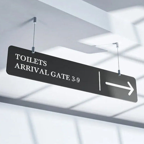 A black hanging signage with white text displaying 'TOILETS ARRIVAL GATE 3-9' suspended indoors, likely in a transportation hub like an airport or train station.
