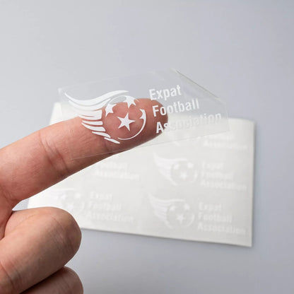 White inked Clear sticker with 'Expat Football Association' text and logo held by a finger against a light gray background