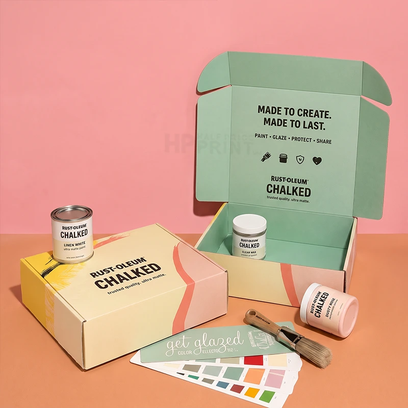 A Rust-Oleum Chalked paint kit displayed with its open mint-green box, a closed cream-colored box, a paint can, a paint tube, a paint brush, and a color swatch card on a peach and pink background.