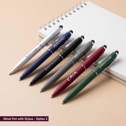 Five metal ballpoint pens in different colors are arranged diagonally on a beige surface next to an open spiral notebook. The pens are silver, navy blue, black, gray, and green, each with custom printed text such as 'bitcore', '#IRISHNICT', 'FOR SURFACE', 'SPEED LINE', and 'CA.