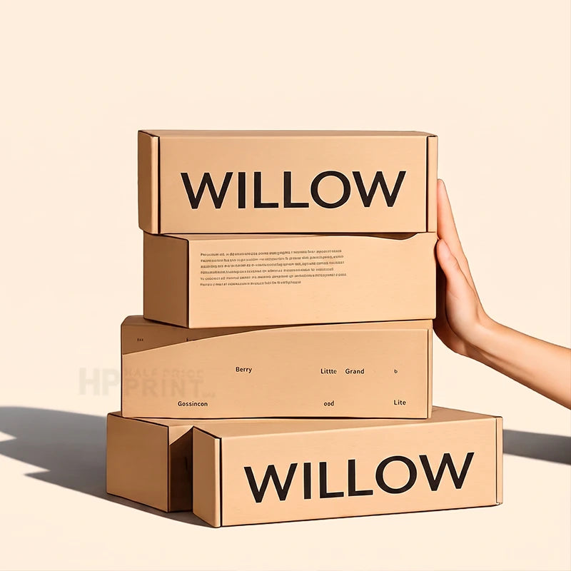 A stack of four kraft paper ecommerce mailer boxes branded with 'WILLOW' in bold black letters, held by a person's hand against a warm beige background.
