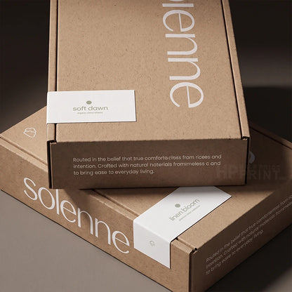 Three brown kraft paper product boxes stacked together on a dark surface. The boxes feature white printed branding and text, including 'solenne' and 'ling bloom', along with small white product tags.
