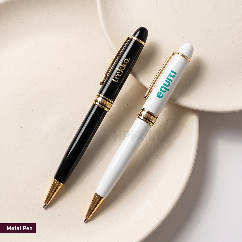 Two metal ballpoint pens are arranged on a light beige ceramic plate. One pen is glossy black with gold trim and the clip shows the brand name 'iretako'.