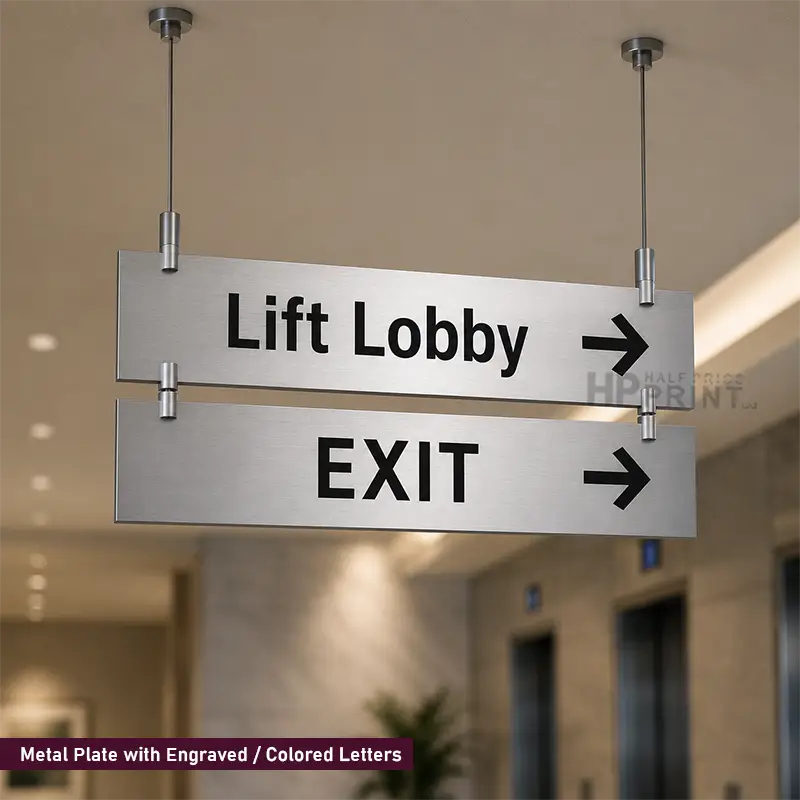 Two horizontal stainless steel directional signs hanging from ceiling fixtures in an indoor lobby. The top sign reads 'Lift Lobby' with a right arrow, and the bottom sign reads 'EXIT' with a right arrow.