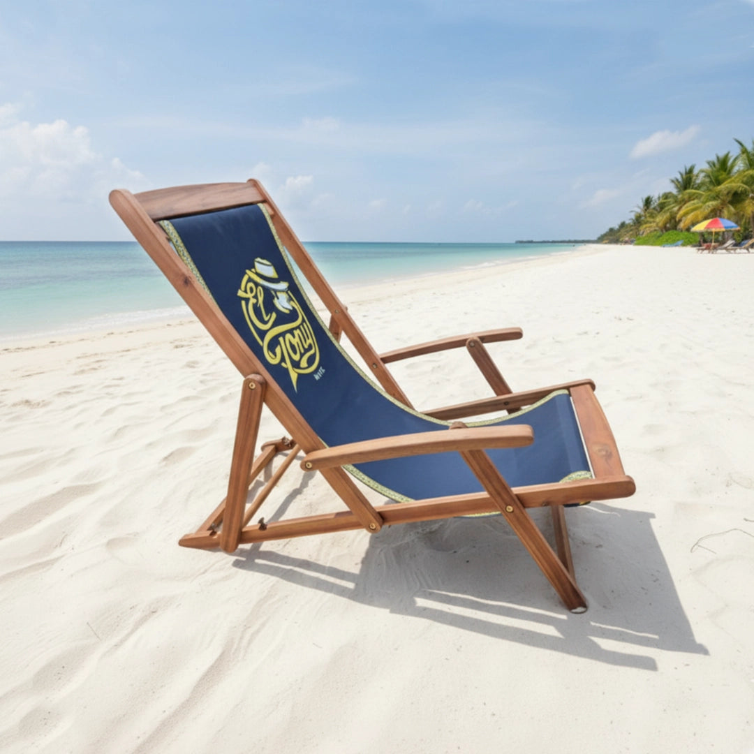 Wooden beach chair with blue cushion on a sandy beach with ocean and palm trees in the background.