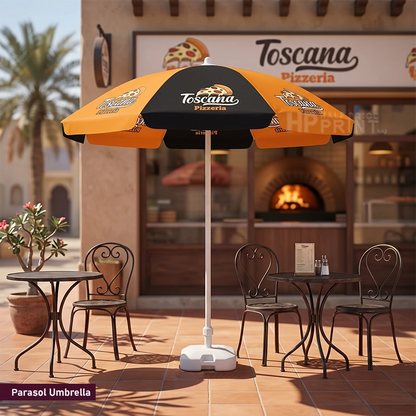 An outdoor parasol umbrella with a black and orange design stands in front of a pizzeria storefront. The umbrella features the text 'Toscano Pizzeria' and pizza graphics, with a white pole and base.