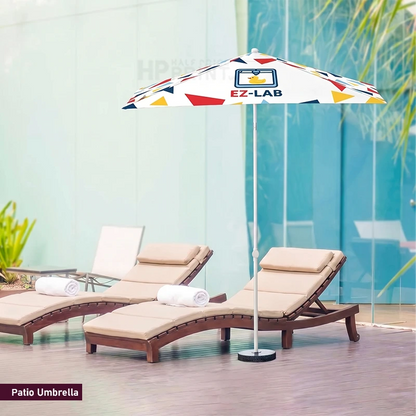 A patio umbrella with a white canopy featuring colorful geometric shapes and the EZ-LAB logo, positioned next to two beige lounge chairs in a modern outdoor setting.